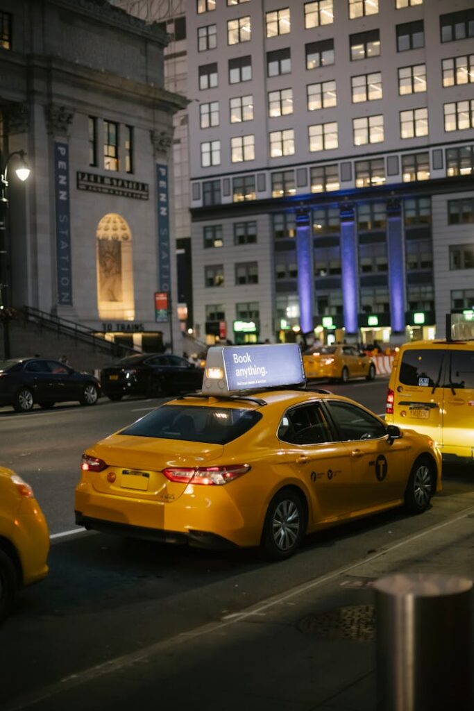 Urban scene on a New York street at night featuring yellow taxis in front of Penn Station.