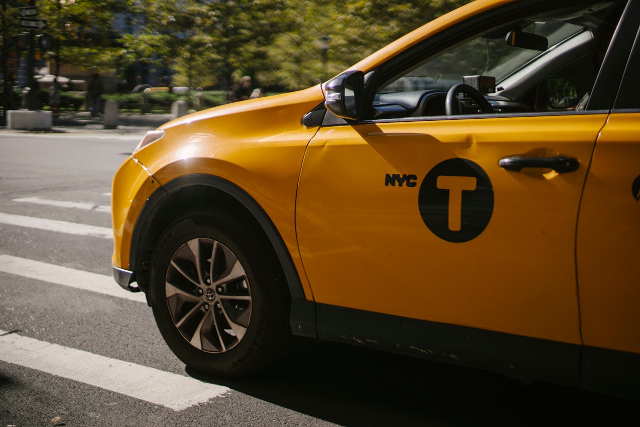 our-story-01 A bright yellow taxi with NYC signage at a crosswalk during the day.